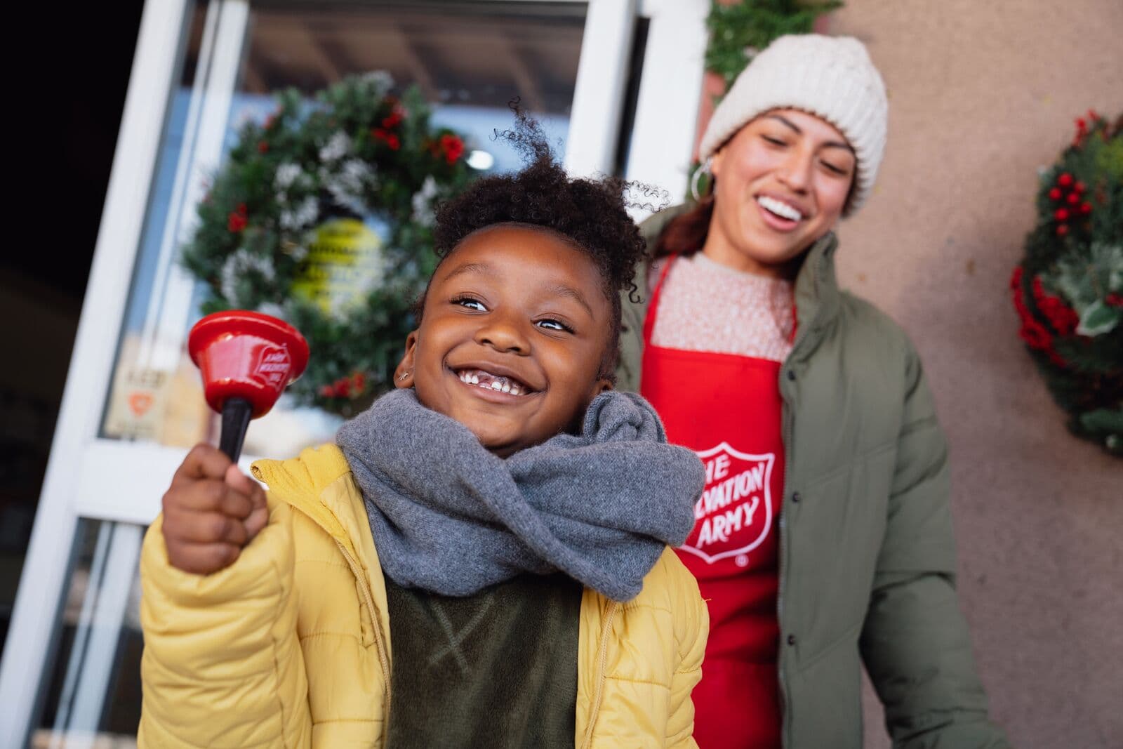 A happy child ringing a bell in front of a Salvation Army kettle.